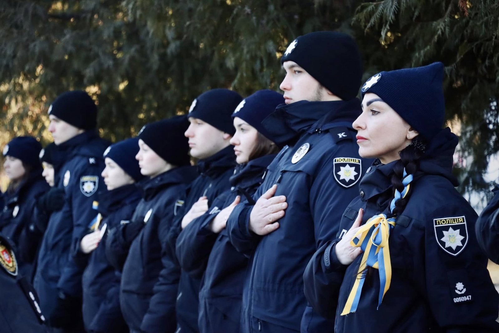 Працівники поліції тримаючи руку на серці, стоять на дворі.